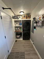 Washroom with hardwood / wood-style floors, a textured ceiling, stacked washing maching and dryer, and electric panel