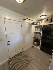 Washroom with hardwood / wood-style floors, stacked washer / drying machine, a textured ceiling, and wooden walls