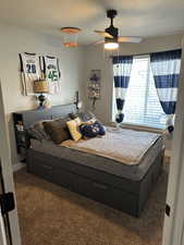 Bedroom with dark colored carpet, ceiling fan, and a textured ceiling