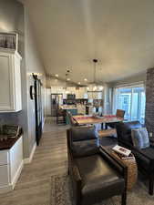 Living room with light hardwood / wood-style floors, an inviting chandelier, a textured ceiling, and vaulted ceiling