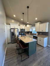 Kitchen featuring pendant lighting, white cabinetry, lofted ceiling, and appliances with stainless steel finishes