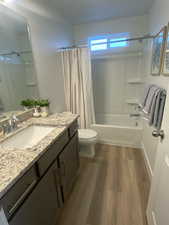 Full bathroom featuring wood-type flooring, vanity, toilet, and shower / bathtub combination with curtain