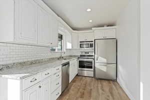 Kitchen featuring decorative backsplash, appliances with stainless steel finishes, sink, white cabinets, and light hardwood / wood-style floors