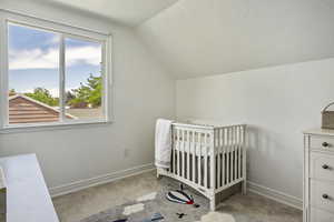 Unfurnished bedroom featuring a crib, light carpet, a textured ceiling, and lofted ceiling