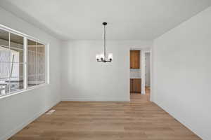 Unfurnished dining area featuring light hardwood / wood-style floors and an inviting chandelier
