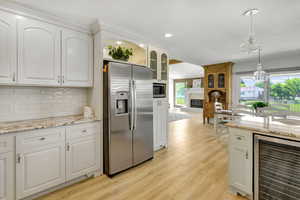 Kitchen featuring appliances with stainless steel finishes, light wood-type flooring, beverage cooler, pendant lighting, and white cabinetry