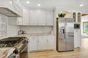 Kitchen with light stone countertops, white cabinetry, light hardwood / wood-style floors, and appliances with stainless steel finishes