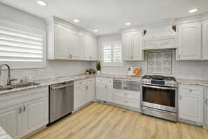 Kitchen featuring appliances with stainless steel finishes, light hardwood / wood-style flooring, white cabinetry, and sink