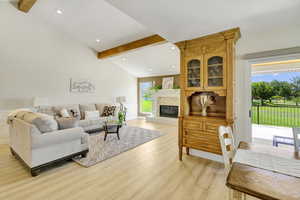 Living room featuring vaulted ceiling with beams, light hardwood / wood-style flooring, and a fireplace