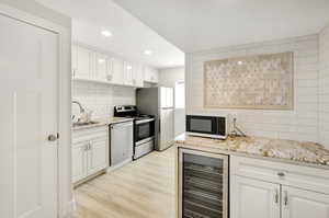 Kitchen featuring appliances with stainless steel finishes, light stone counters, beverage cooler, light hardwood / wood-style flooring, and white cabinets