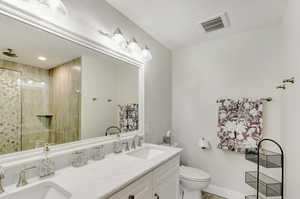 Bathroom featuring tiled shower, vanity, and toilet