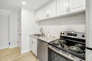 Kitchen featuring white cabinetry, tasteful backsplash, light stone counters, light hardwood / wood-style flooring, and appliances with stainless steel finishes