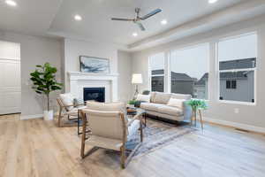 Living room featuring ceiling fan, a raised ceiling, and light wood-type flooring