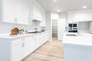 Kitchen with custom exhaust hood, light hardwood / wood-style flooring, stainless steel appliances, decorative backsplash, and white cabinets