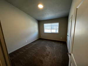 Unfurnished room with dark carpet and a textured ceiling