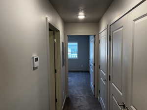 Hall featuring a textured ceiling and dark colored carpet