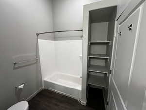 Bathroom with hardwood / wood-style floors, shower / bath combination, and toilet