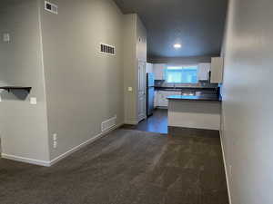 Kitchen with dark colored carpet, appliances with stainless steel finishes, white cabinetry, and sink