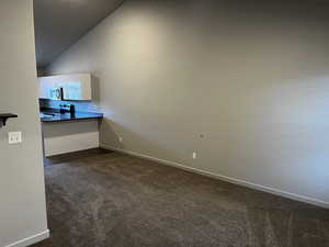 Empty room featuring dark carpet and lofted ceiling