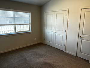 Unfurnished bedroom featuring carpet floors, vaulted ceiling, and a closet