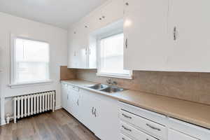 Kitchen with radiator heating unit, white cabinets, light wood-type flooring, and sink