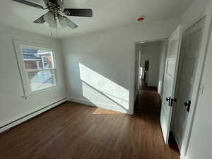 Empty room featuring dark hardwood / wood-style floors, ceiling fan, and baseboard heating