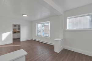 Unfurnished room with plenty of natural light, dark wood-type flooring, and a baseboard heating unit