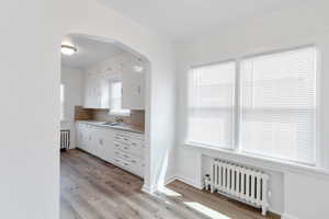 Kitchen featuring radiator, sink, white cabinets, and light hardwood / wood-style floors