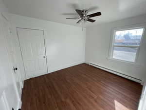 Empty room featuring ceiling fan, dark wood-type flooring, and a baseboard heating unit