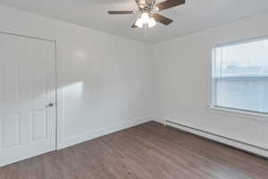 Empty room featuring hardwood / wood-style flooring, ceiling fan, and baseboard heating