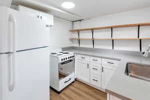 Kitchen featuring white cabinets, white appliances, light hardwood / wood-style floors, and sink