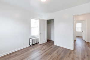 Unfurnished bedroom with multiple windows, a closet, radiator heating unit, and light hardwood / wood-style flooring