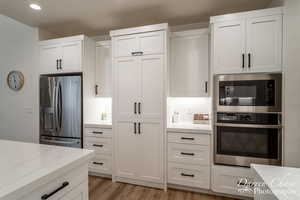 Kitchen featuring light stone countertops, white cabinets, light wood-type flooring, and appliances with stainless steel finishes