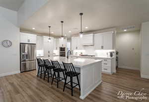 Kitchen with stainless steel appliances, white cabinetry, a kitchen island with sink, and sink