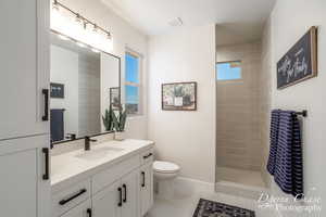 Bathroom featuring tile patterned flooring, plenty of natural light, a tile shower, and vanity