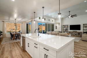 Kitchen featuring a center island with sink, light stone counters, sink, and hanging light fixtures