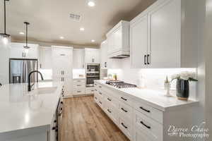 Kitchen with pendant lighting, a kitchen island with sink, sink, appliances with stainless steel finishes, and white cabinetry