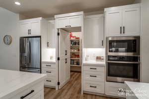 Kitchen featuring white cabinets, light stone counters, light wood-type flooring, and appliances with stainless steel finishes