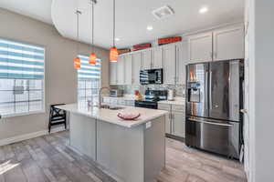 Kitchen featuring appliances with stainless steel finishes, a kitchen island with sink, sink, light hardwood / wood-style floors, and hanging light fixtures