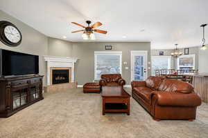 Living room featuring ceiling fan with notable chandelier, light carpet, and a tiled fireplace