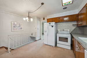 Kitchen with a textured ceiling, white appliances, light colored carpet, decorative light fixtures, and an inviting chandelier