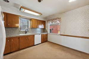 Kitchen with a textured ceiling, white appliances, light colored carpet, and sink