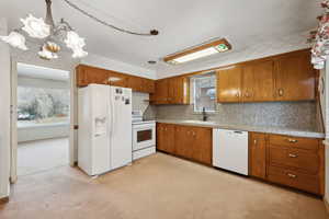 Kitchen featuring white appliances, light carpet, a wealth of natural light, and an inviting chandelier