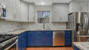 Kitchen featuring light stone countertops, appliances with stainless steel finishes, tasteful backsplash, sink, and light hardwood / wood-style floors