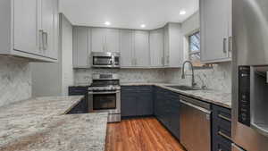 Kitchen featuring light hardwood / wood-style floors, light stone counters, sink, and appliances with stainless steel finishes