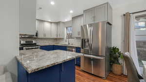 Kitchen featuring kitchen peninsula, appliances with stainless steel finishes, light stone counters, sink, and light hardwood / wood-style floors