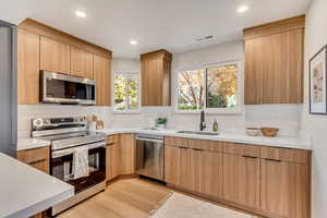 Kitchen featuring light brown cabinets, light wood-type flooring, sink, and appliances with stainless steel finishes