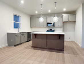 Kitchen featuring pendant lighting, gray cabinets, appliances with stainless steel finishes, and light hardwood / wood-style flooring