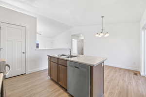 Kitchen featuring dishwasher, sink, vaulted ceiling, decorative light fixtures, and a kitchen island with sink
