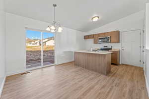 Kitchen with light wood-type flooring, stainless steel appliances, sink, hanging light fixtures, and lofted ceiling